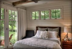 a bed sitting in a bedroom next to a window with curtains and pillows on it