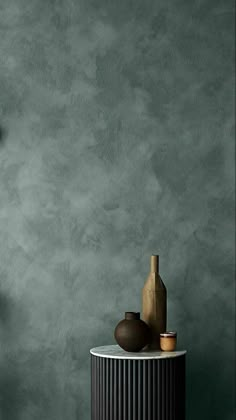 a vase sitting on top of a white table next to a wall with a clock