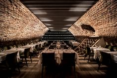 an empty restaurant with tables and chairs in front of a brick wall that has wine bottles on it