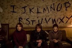 three young men sitting on a couch in front of a wall with letters written on it