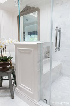 a white bathroom with a walk in shower next to a stool and mirror on the wall