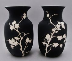 two black vases with white flowers and leaves painted on the sides, one is larger than the other