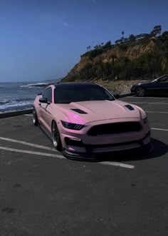 a pink car parked in a parking lot next to the ocean