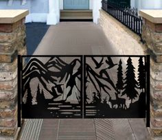 an iron gate with mountains and trees on the front entrance to a house that is surrounded by stone pillars