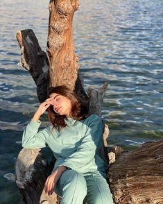 a woman sitting on top of a tree next to the ocean with her eyes closed