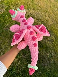 a person holding a pink crocheted giraffe toy in their hand on the grass