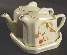 a white tea pot and saucer with leaves on it sitting on a black surface