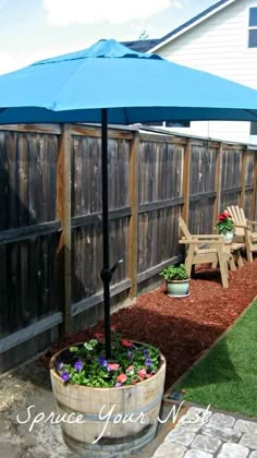 an umbrella and some chairs in a back yard near a wooden fence with grass on the ground