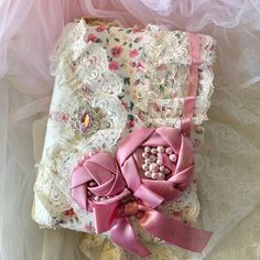 an old book covered in lace and pink ribbon with pearls on the cover, sitting on a bed