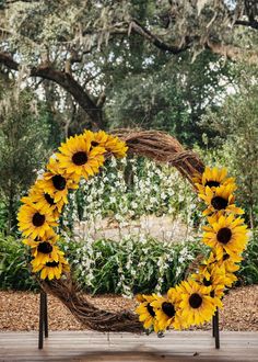 a wreath with sunflowers on it sitting in front of some trees and bushes