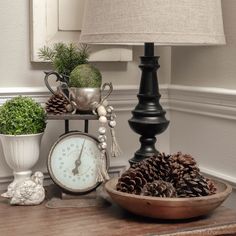 a table with a clock, pine cones and other items on it next to a lamp