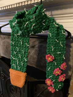 a crocheted green scarf with flowers hanging from it's end next to a fireplace