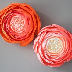 two paper flowers sitting next to each other on a gray surface with white and orange petals