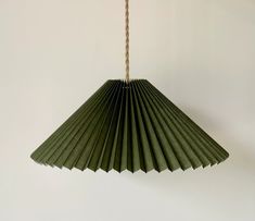 a green paper fan hanging from a rope on a wall with white walls in the background