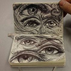 a hand holding an open notebook with drawings on the pages and eyeballs in it