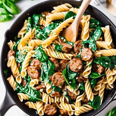 sausage and spinach pasta in a skillet with a wooden spoon on the side