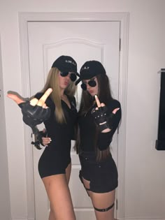 two women dressed in black posing for the camera with their fingers up and pointing at them