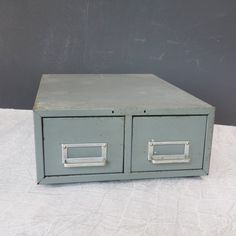 an old gray metal filing cabinet on a white cloth covered tablecloth with two drawers