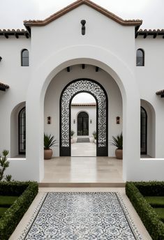 an entrance to a white house with blue and white tiles on the floor, hedges in front