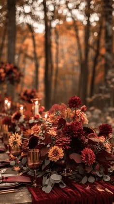 a table topped with lots of red and orange flowers next to candles in the woods