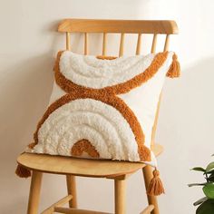 an orange and white pillow sitting on top of a wooden chair next to a potted plant