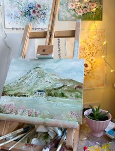 an artist's easel with paint and flowers on it in front of paintings