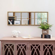 a sideboard with books and plants on it in front of a mirror