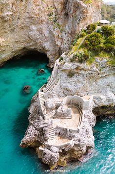 an aerial view of the blue water and steps leading to a cave on top of a cliff