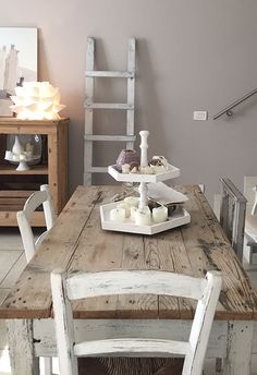 a wooden table with white chairs and candles on it in front of a gray wall