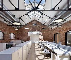 an empty office with white desks and chairs in front of brick walls, windows and skylights