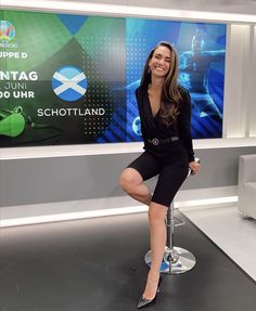 a woman sitting on top of a stool in front of a tv screen and posing for the camera