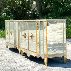 three mirrored sideboards with gold trim and scalloped edges in front of trees