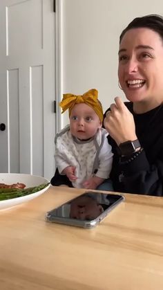 a woman sitting at a table with a baby in front of her and a plate of food on the table