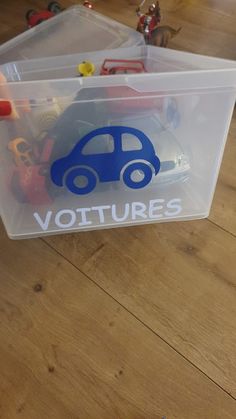 a plastic container filled with toy cars on top of a wooden floor next to toys