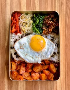 an egg on top of rice and vegetables in a metal container