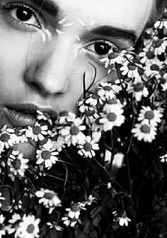 a black and white photo of a woman with daisies in her hair looking at the camera