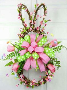 a wreath with pink and green bows hanging on the front door, decorated with flowers