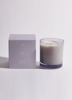 a candle sitting next to a box on a white surface with the lid open and it's lit