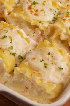 a casserole dish with chicken, cheese and sauce in it on a wooden table