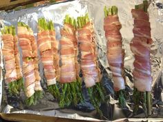 asparagus wrapped in bacon on top of aluminum foil lined with other food items