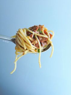 a spoon full of pasta with meat and cheese on it is being held in the air