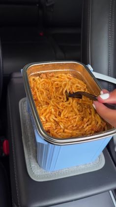 a person is holding a fork over a container of noodles in the back seat of a car