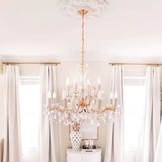 a chandelier hanging from the ceiling in a room with white curtains and drapes