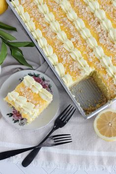 a lemon cake with white frosting on a plate next to a fork and knife