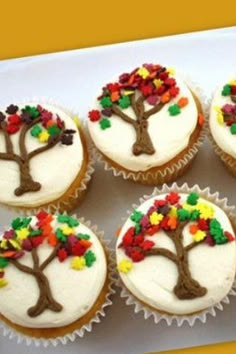 cupcakes decorated with trees and leaves on top of a white platter filled with frosting