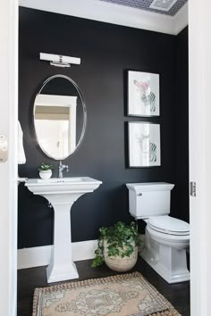 a white toilet sitting next to a sink in a bathroom under a mirror and framed pictures on the wall