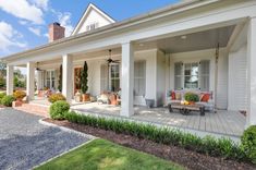 the front porch of a white house with lots of furniture on it's patio