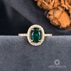 an oval shaped emerald and diamond ring on top of a gray velvet pillow with a flower in the background