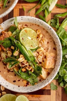 two white bowls filled with soup and garnished with limes, peanuts and cilantro