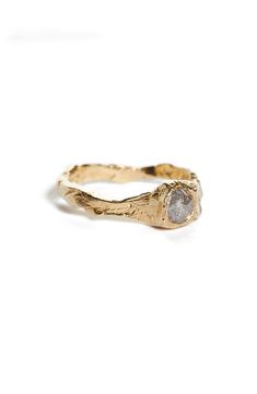 a gold ring with a white diamond in the center on a white background, it is made out of wood and has a rough textured surface